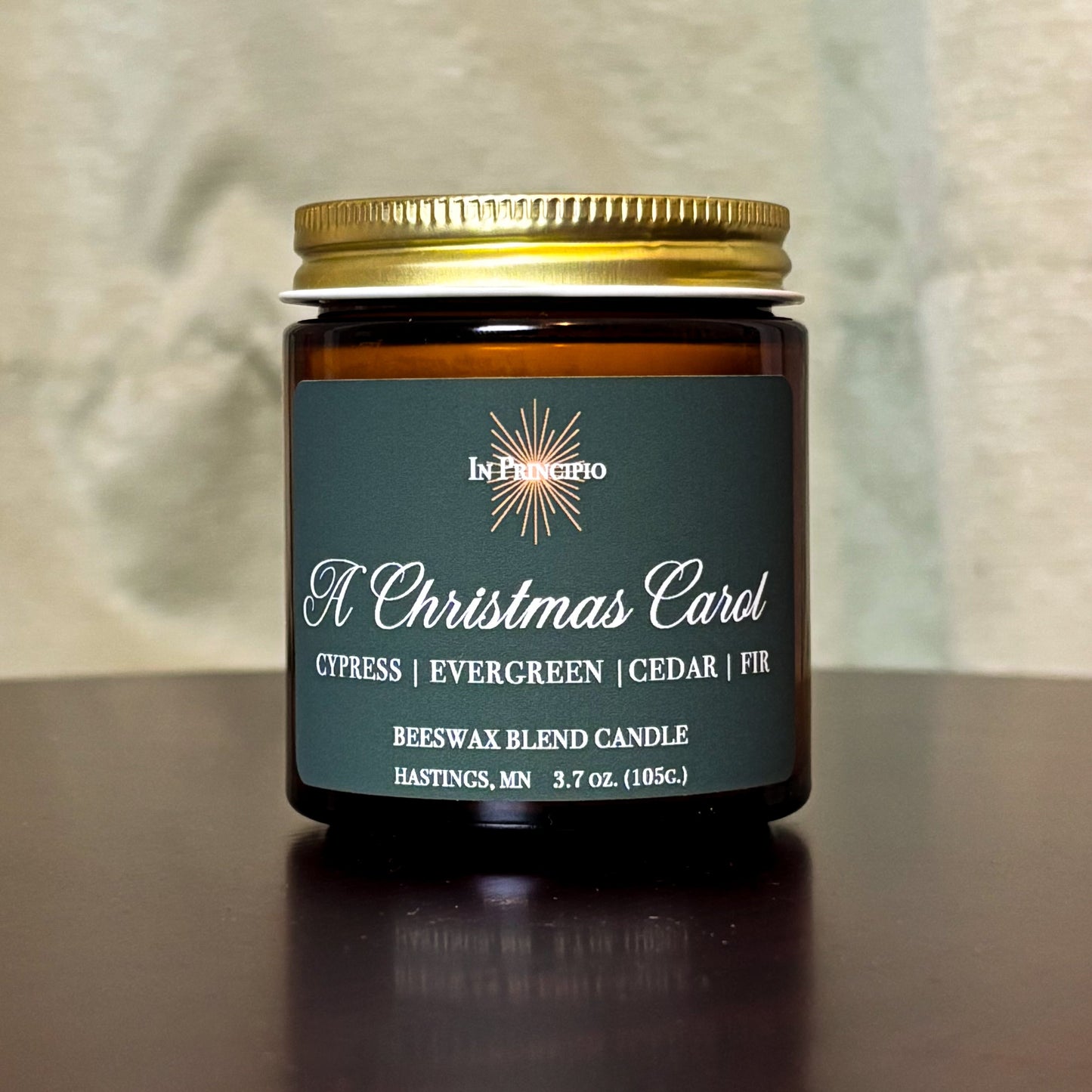 A Christmas Carol mini container candle with a gold lid on a wooden surface.
