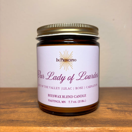Beeswax blend candle labeled 'Our Lady of Lourdes' by In Principio on a wooden surface.